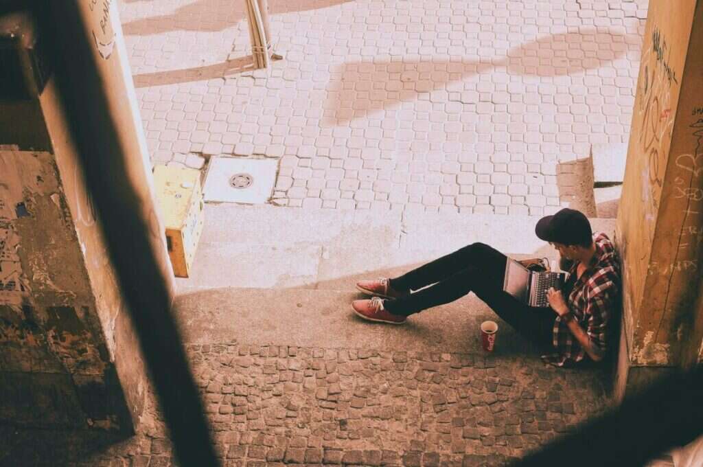A guy using a laptop in a corner an of alley